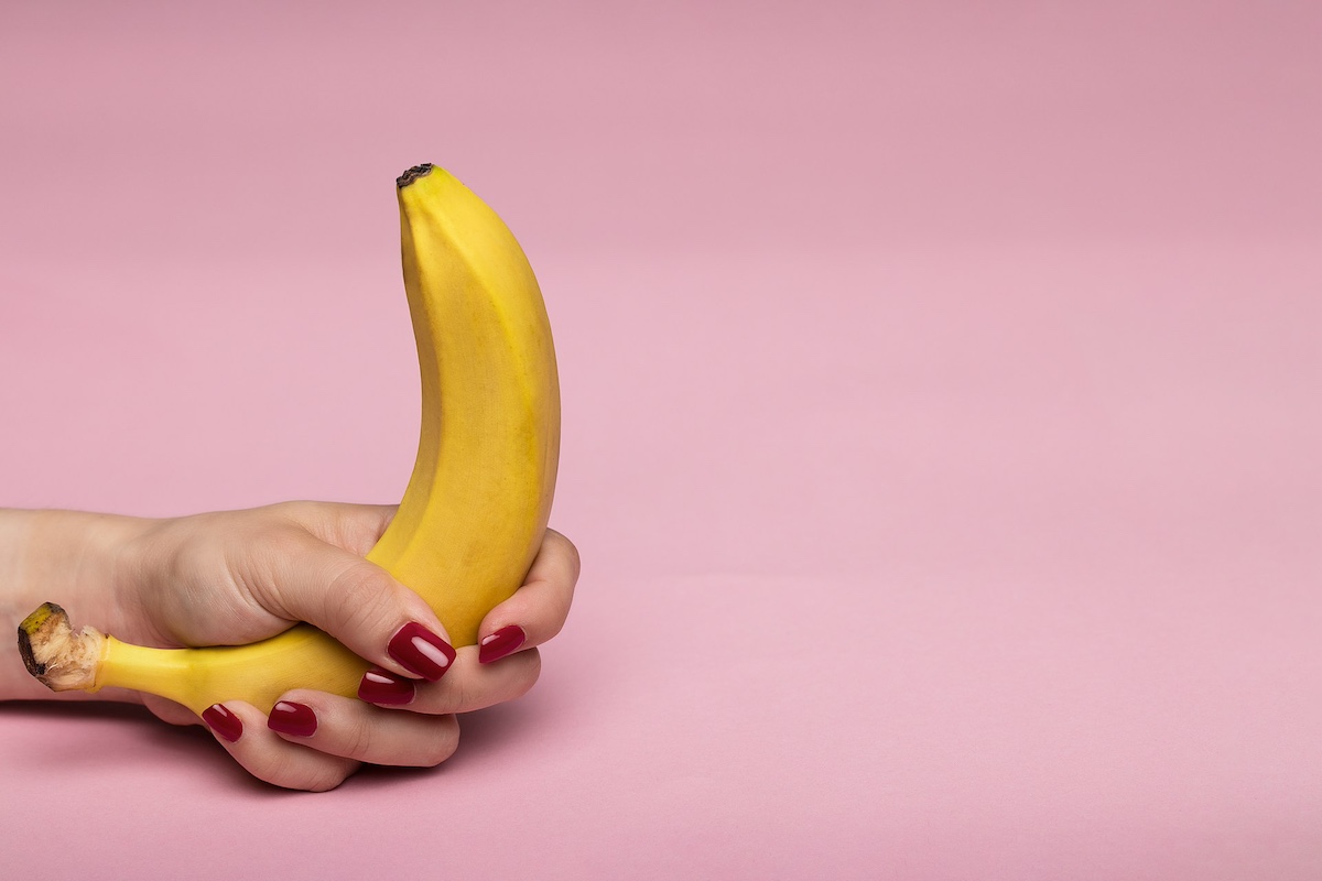 mano afferra banana su sfondo rosa