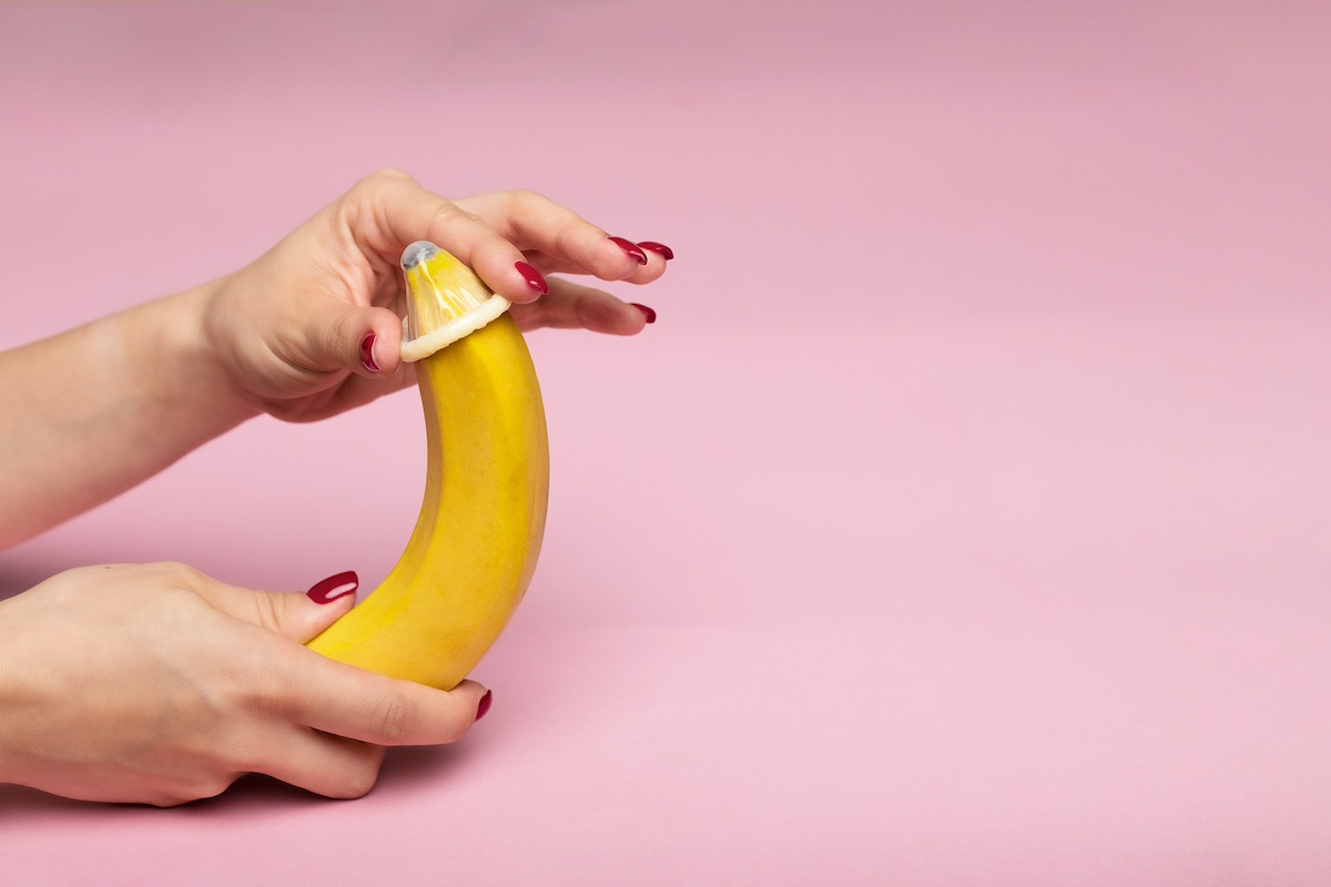 mani femminili mettono preservativo a una banana con sfondo rosa