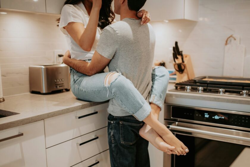 Un uomo abbraccia dolcemente una donna in una cucina moderna, in un momento di affetto e complicità, con luce naturale calda