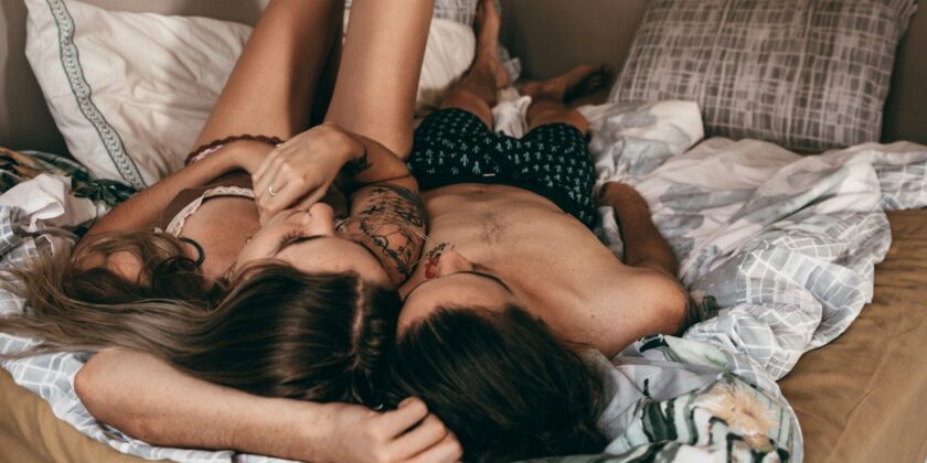 Una coppia eterosessuale sdraiata sul letto in un momento di intimità e relax, illuminata da luce naturale calda, in un ambiente accogliente e tranquillo.