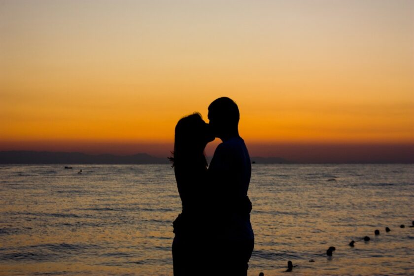 Coppia che si bacia davanti a uno specchio d’acqua al tramonto