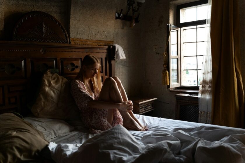 Giovane donna seduta sul bordo del letto, pensierosa, immersa nei propri pensieri