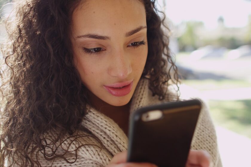 Immagine a tema dirty talk: mani con smartphone e schermata chat sfocata, luce calda e atmosfera rilassata.
