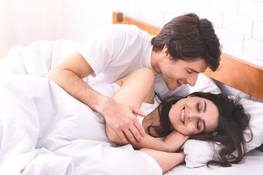 Immagine a tema orgasmo femminile: coppia in intimità non esplicita, abbraccio morbido e luce naturale del mattino.