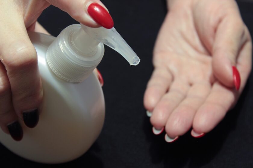 Immagine a tema sesso anale: mano che applica gel trasparente sulle dita, luce calda e stile minimal.