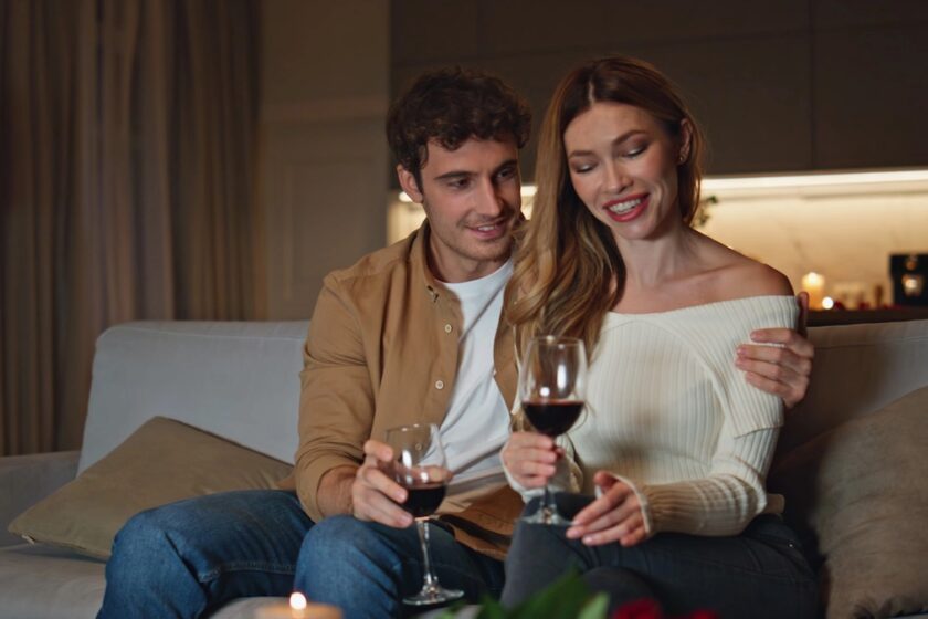 Immagine a tema sesso in coppia: coppia sul divano in dialogo intimo e rilassato, mani vicine, luce calda serale.