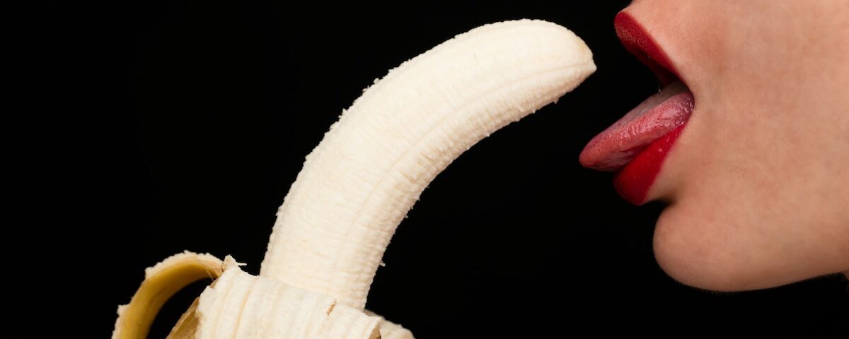 Persona tiene una banana vicino alla bocca con lingua fuori in stile ironico e provocatorio