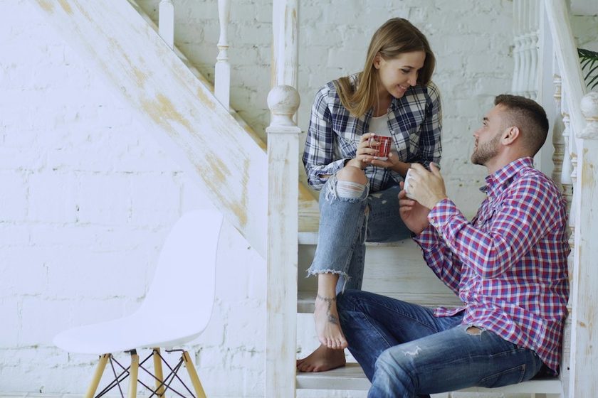 Coppia seduta sulle scale di casa che conversa tenendo in mano due tazze.
